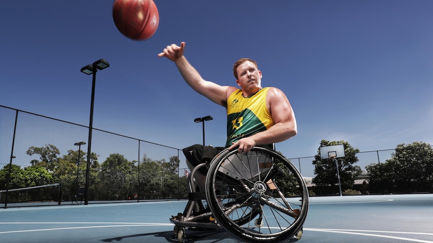 Paralympian Matt McShane wears a green and gold singlet in his wheelchair and shoots a basketball 