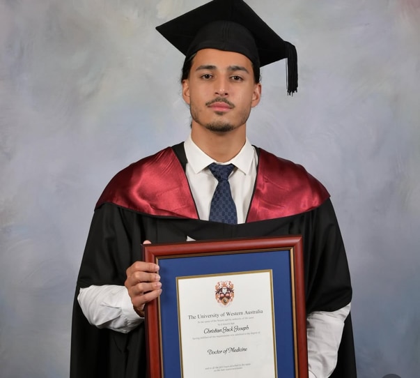 Mr Joseph wearing a graduating gown and holding frame