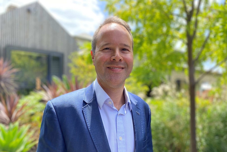 Jonathan Spear smiles in front of a leafy background.