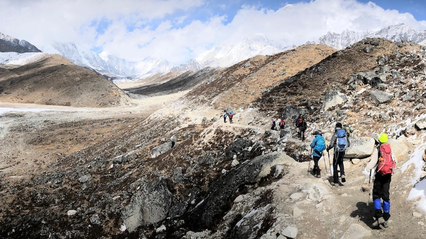 Trekkers carry hiking packs with mountains in the distance. 