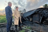 A man and a woman stand amidst the ruins of a farm destroyed by a bushfire.