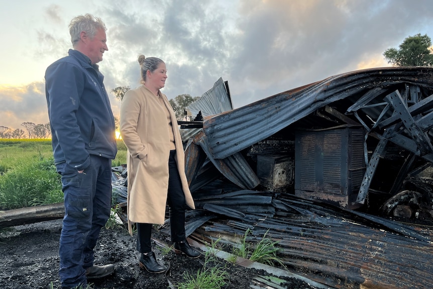 Vyras ir moteris stovi tarp ūkio griuvėsių, kuriuos sunaikino krūmų gaisras.