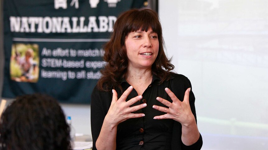 A woman with dark hair gestures with her hands as she speaks.