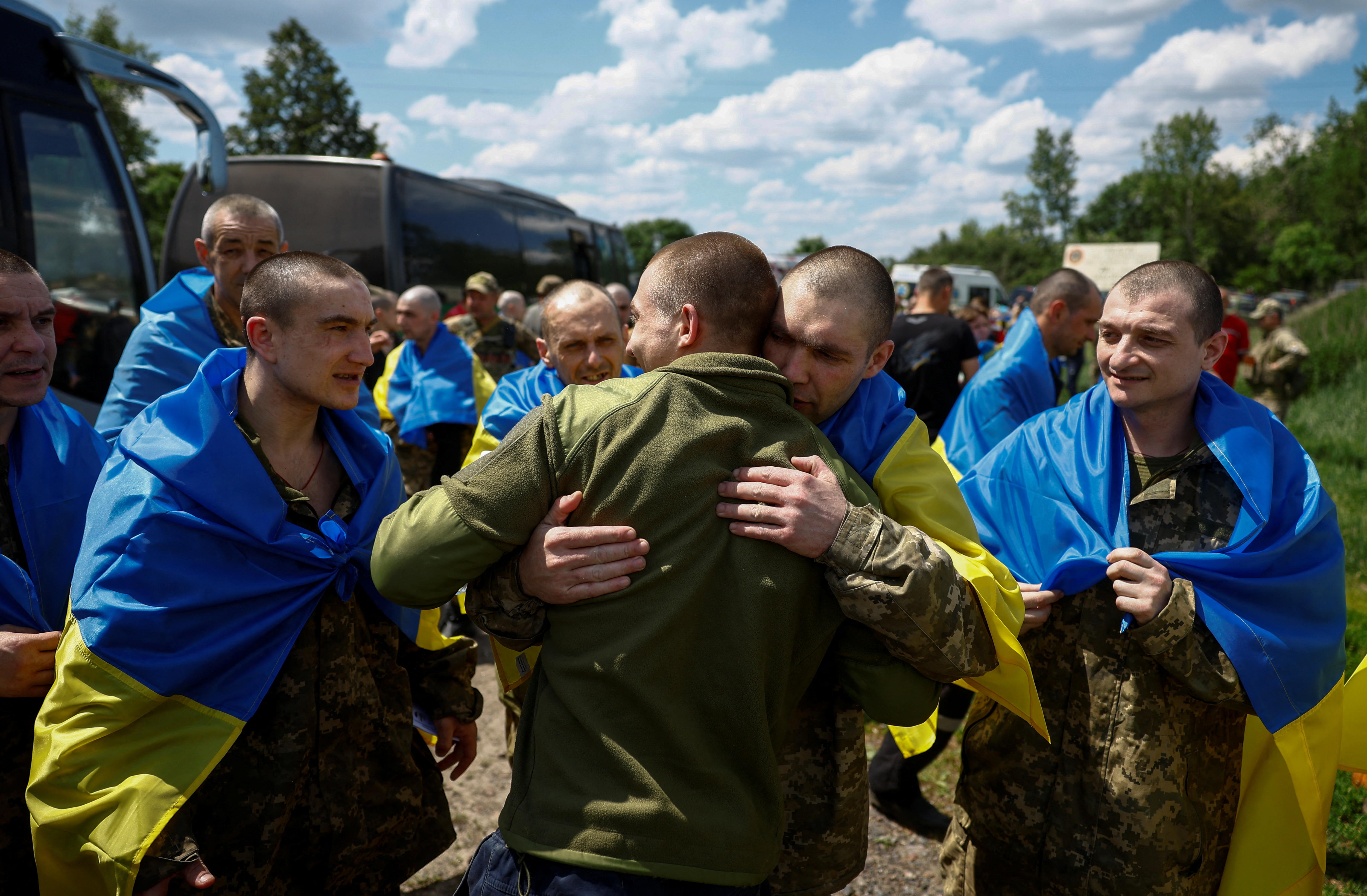 Man wearing green Army uniform embraces released prisoner draped in Ukraine flag