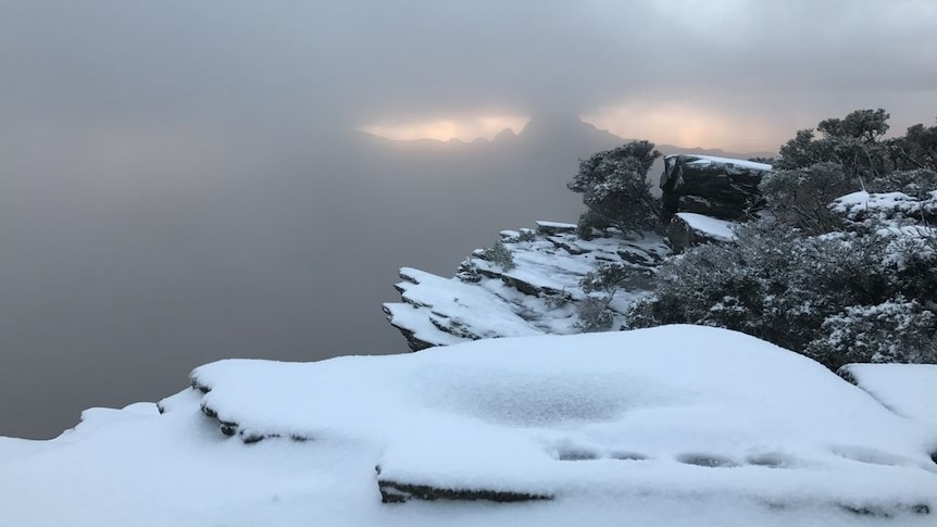 A mountain range blanketed in snow with dim light shining through on the horizon.