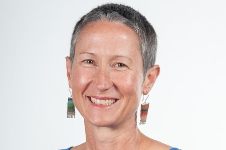 A woman with short, grey hair and large earrings, smiling.
