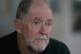 An older man with close-cropped hair and a neat beard, wearing black.