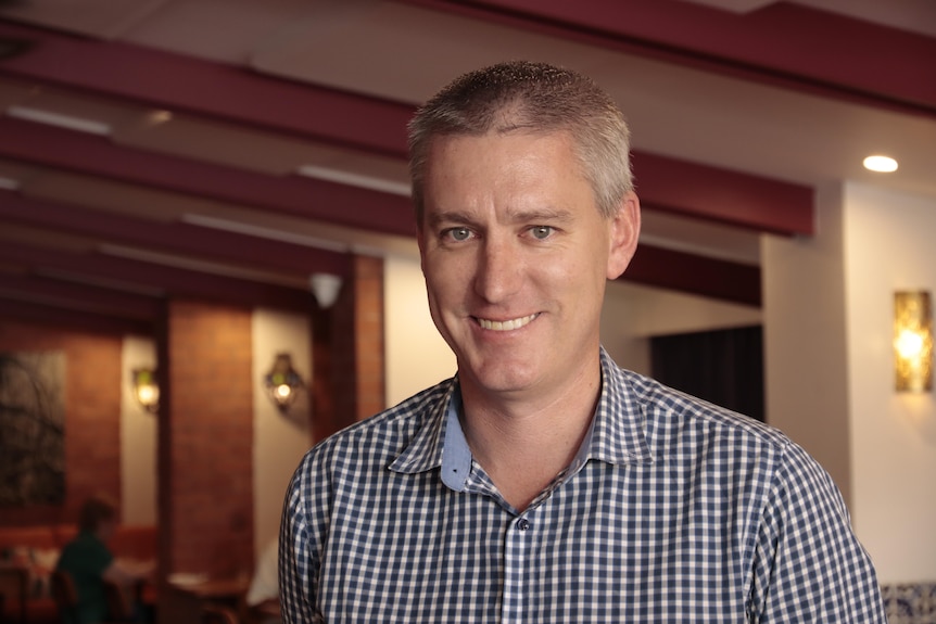 A man wearing a business shirt is standing in a restaurant and smiling to the camera