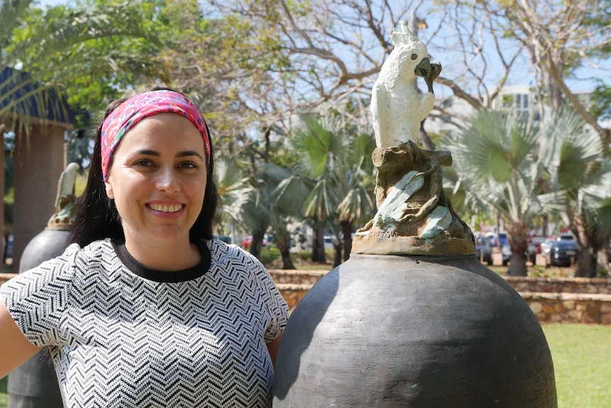Woman in bright headband standing next to statue of cockatoo.