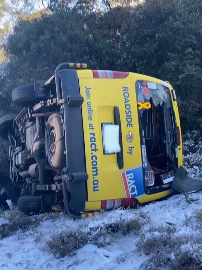 A yellow RACT van is on its side with a broken back window. The ground is snowy and icy.