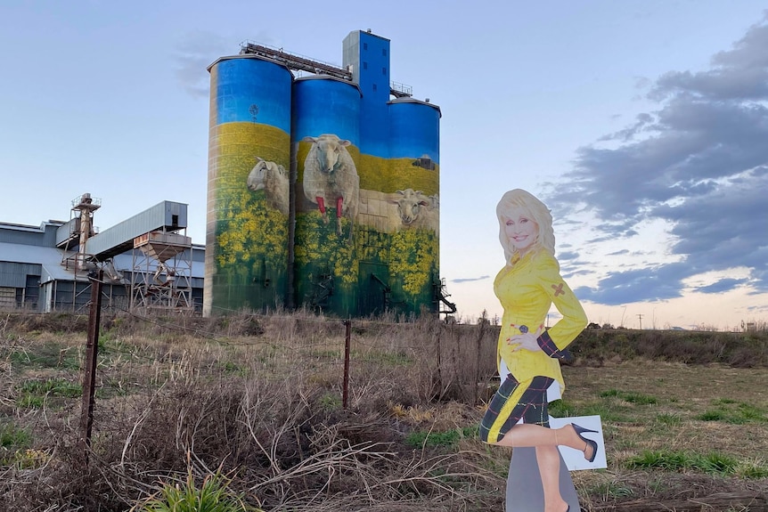 A cardboard cut out of Dolly Parton in front of painted silos in country NSW.