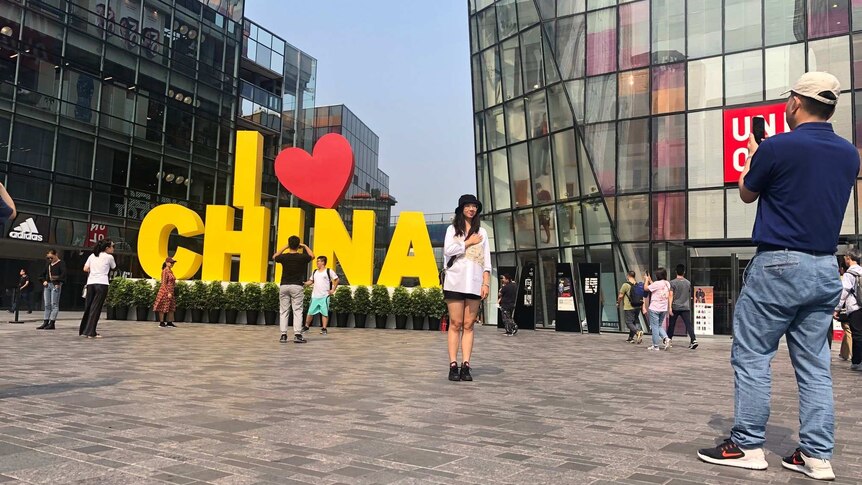 At least five people are seen posing by a sign that reads "I love China" which is yellow, with the "love" being a red heart.
