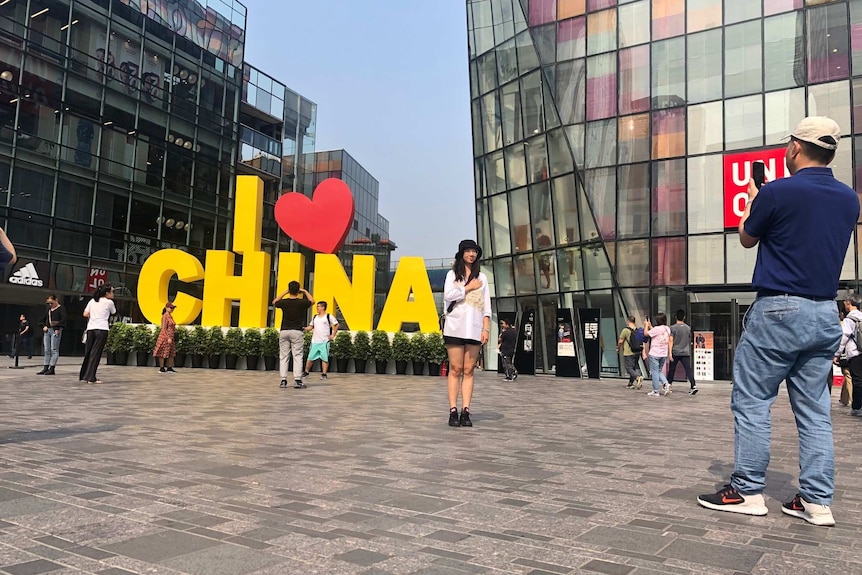 At least five people are seen posing by a sign that reads "I love China" which is yellow, with the "love" being a red heart.