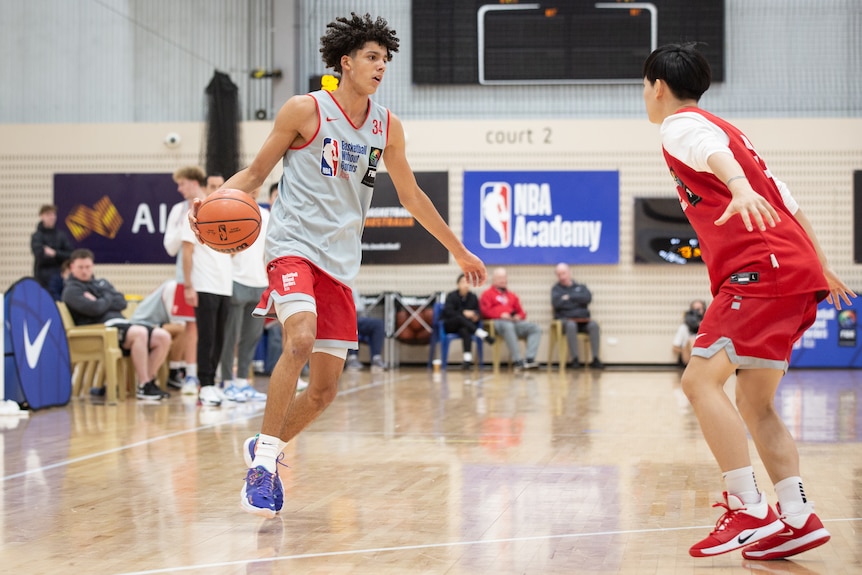 Two young men play basketball on an indoor court.