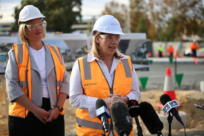 WA Transport Minister Rita Saffioti at a media conference, in an orange hi-vis vest and white hard hat, with another woman.