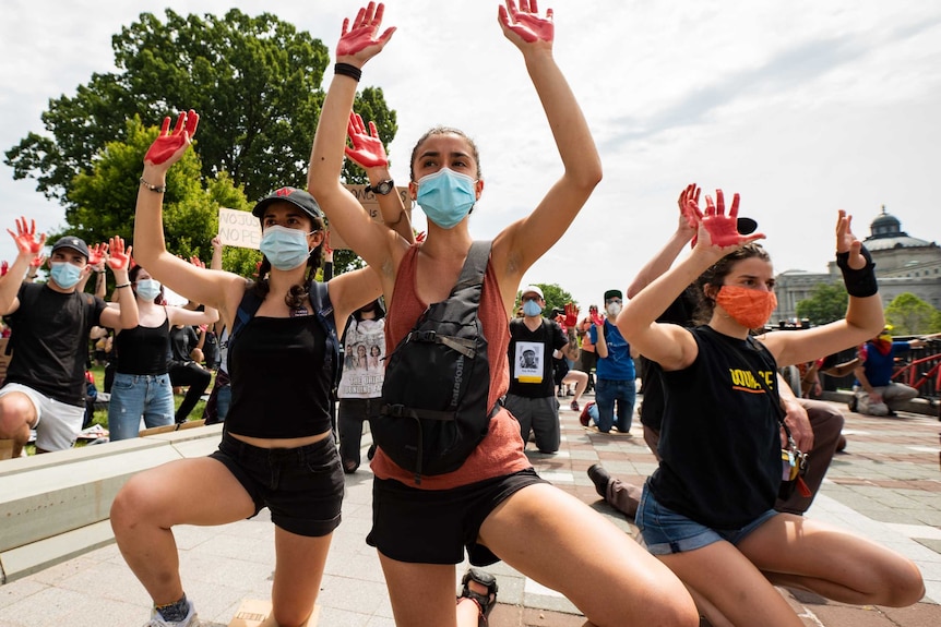 Protesters kneeling with red paint on their hands