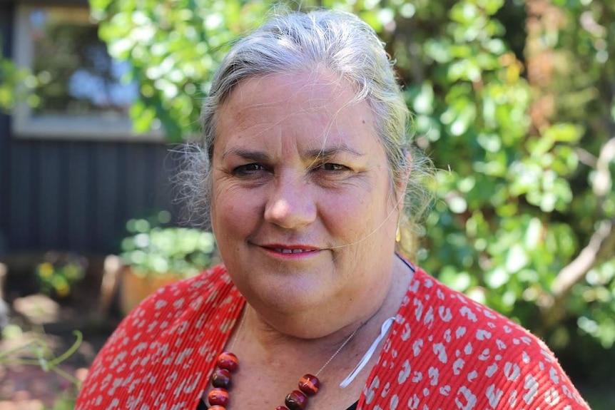 Catherine Chamberlain looks to the camera, standing in a sunlit garden.