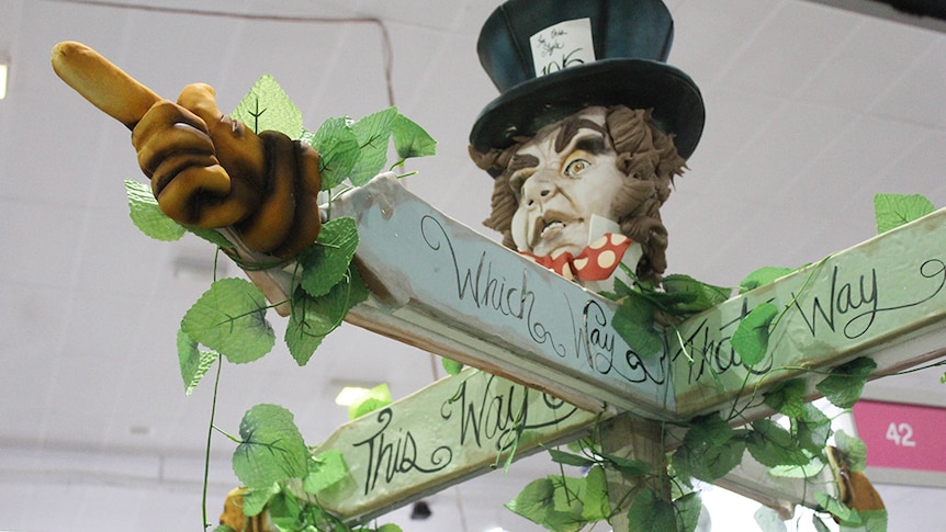 A sugar sculpture of Alice in Wonderland's Mad Hatter in a top hat, with his hands out like a sign post.