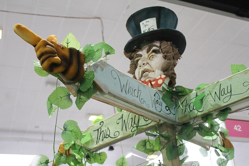 A sugar sculpture of Alice in Wonderland's Mad Hatter in a top hat, with his hands out like a sign post.