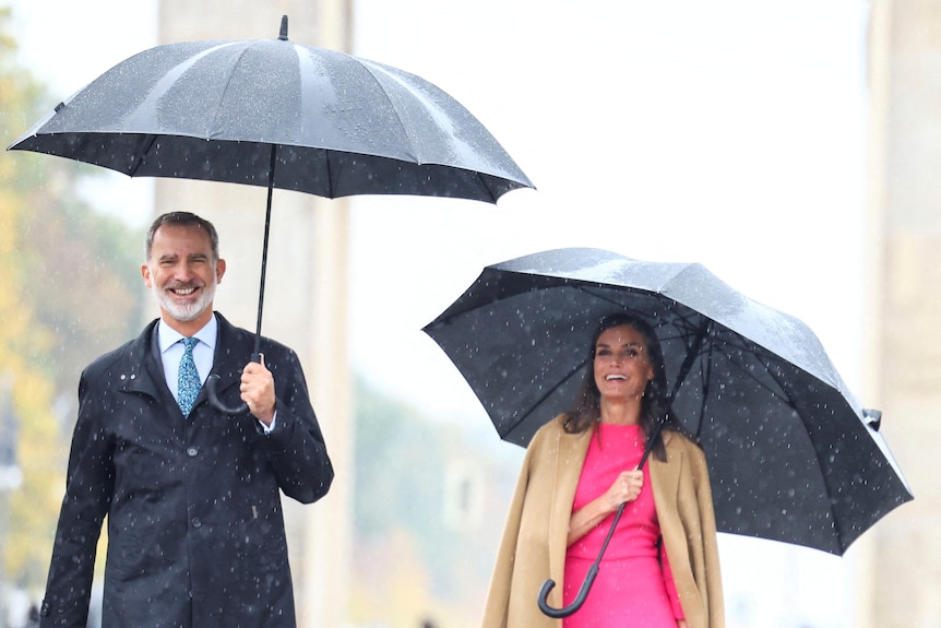 A man and a woman walk through rain carrying big black umbrellas 