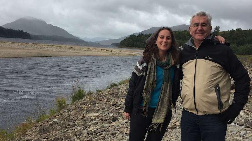 Katie Lees and her father Ian stand with their arms around each other and smiling in front of a lake.