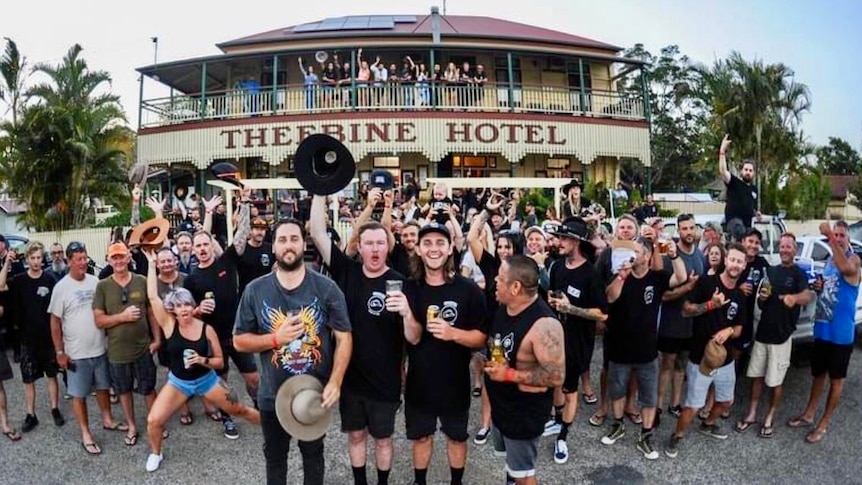 A big crowd of people cheering as they stand in front of the historic Theebine Hotel.