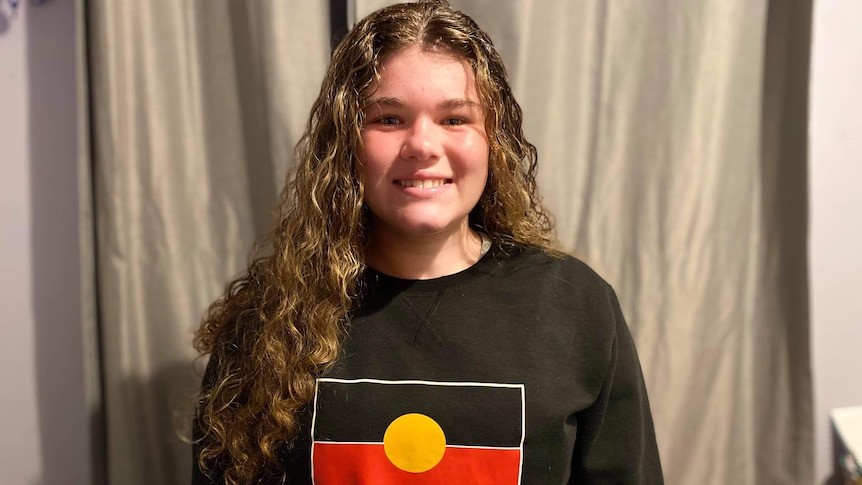 A teenager wearing a black jumper with the aboriginal flag