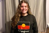A teenager wearing a black jumper with the aboriginal flag