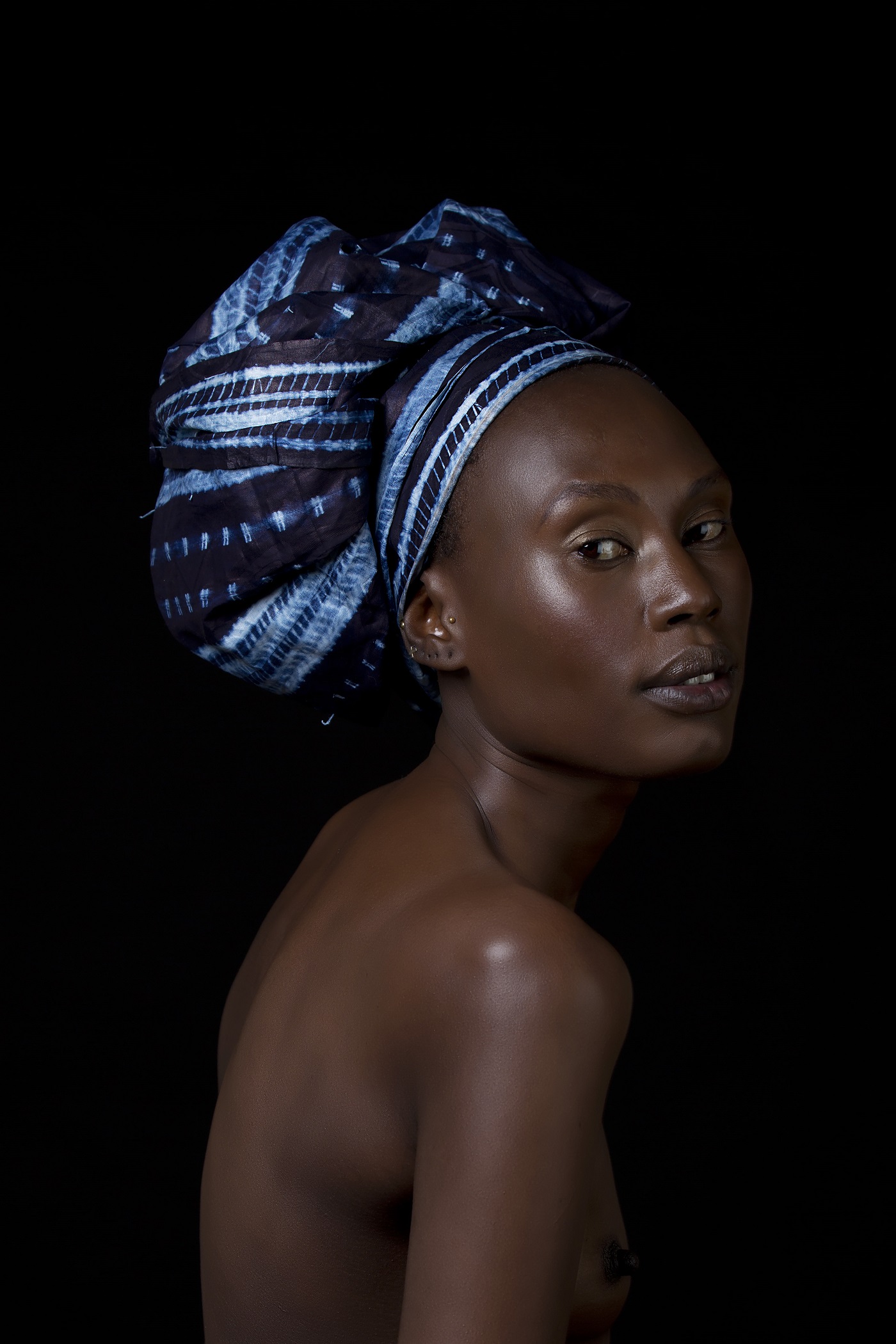 A woman, naked except for a blue turban, in a dark portrait.