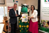 Two people stand with a dinosaur mascot holding new childcare regulations