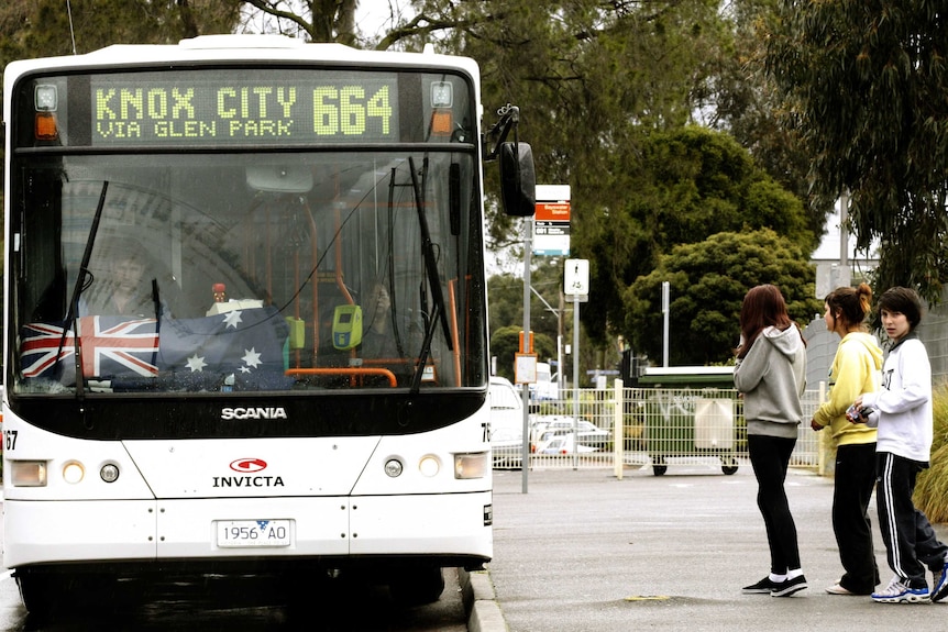 A woman stands on the footpath watching and waiting for a bus approaching the stop in Melbourne.