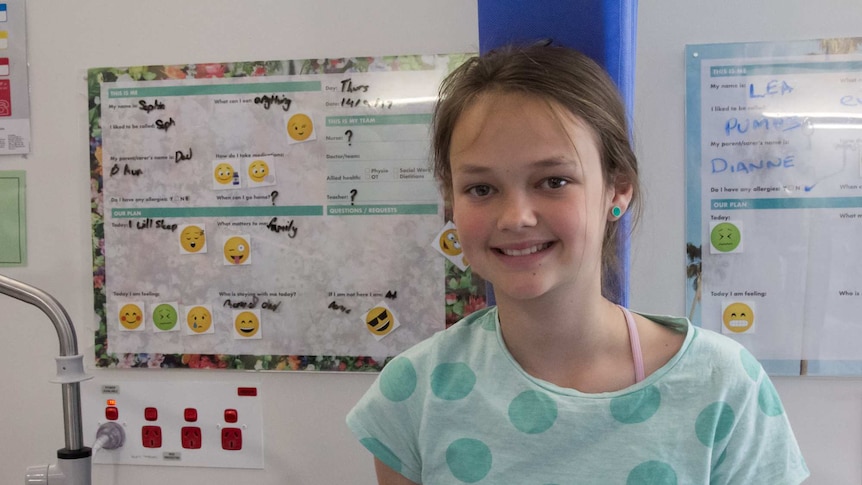 Patient Sophie standing in front of the emoji boards at the Sydney Children's Hospital, Randwick