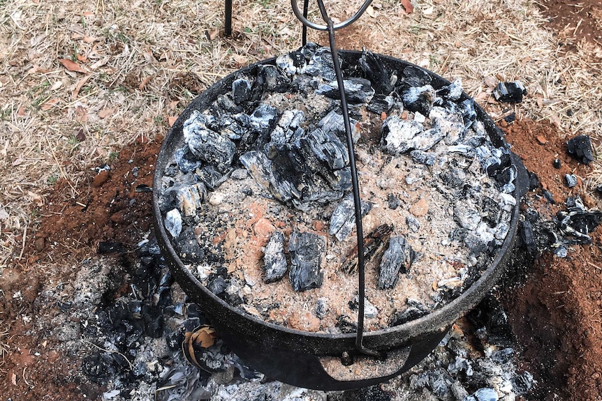 Cast iron camp oven sits in the coals of a bush 'kitchen'.