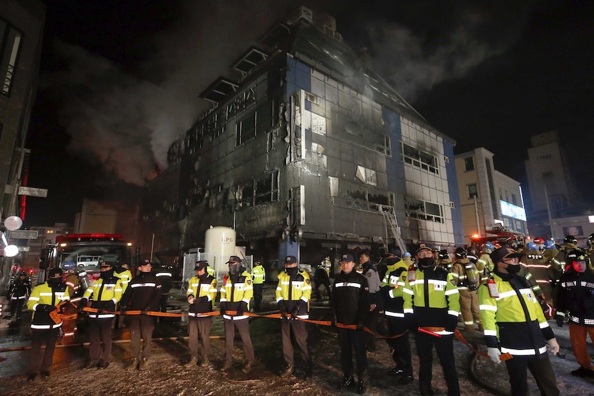 Smoke rises from the building as police officers stand guard outside.