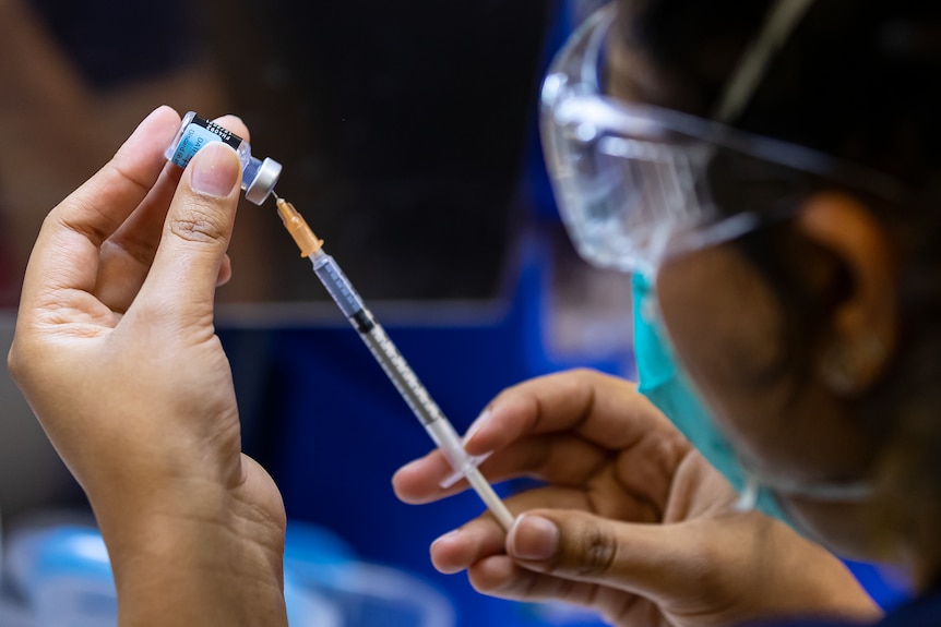 A nurse putting a needle into a small vial.