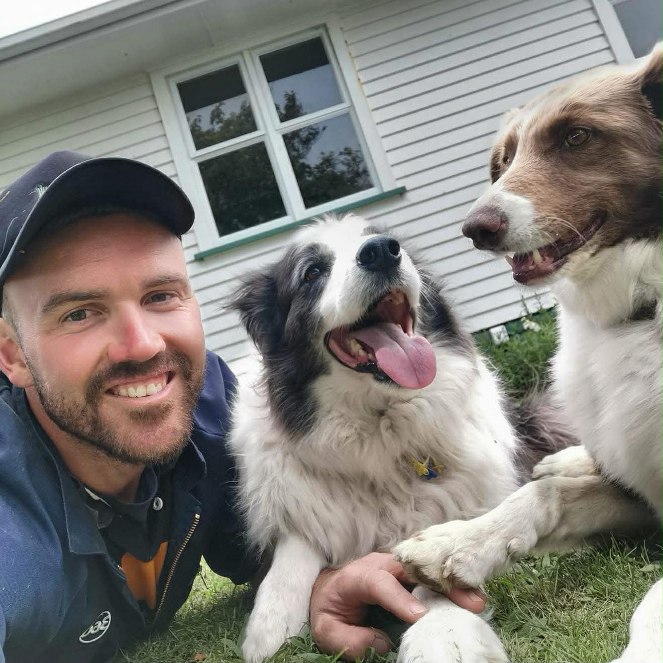 Un joven con gorra en el césped junto a un border collie sonriente