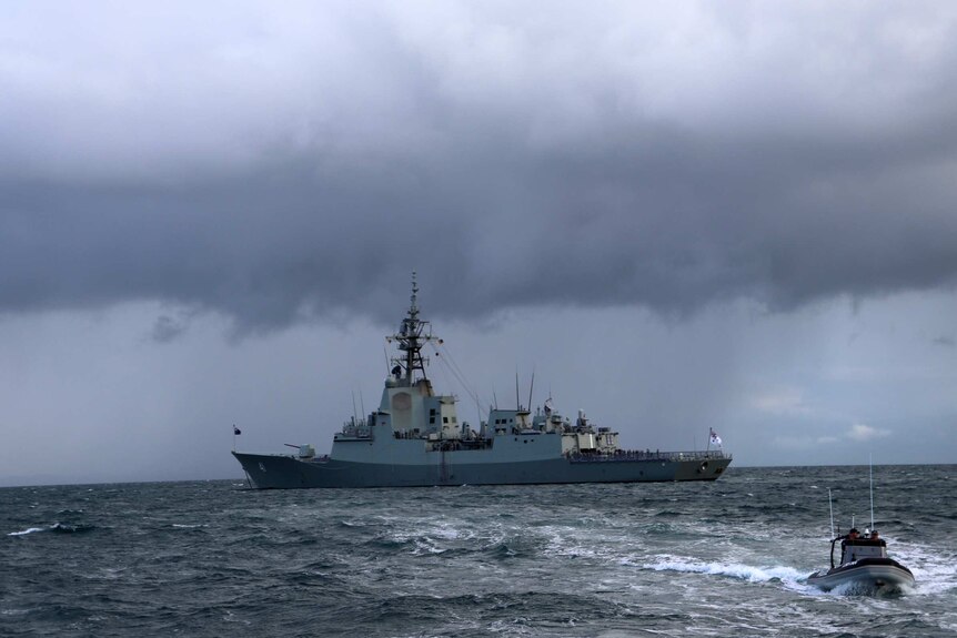 HMAS Brisbane with dark clouds behind it.