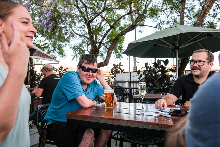 Conor and three friends are pictured around an outside bar table. There's drinks on the table, with trees in the background.