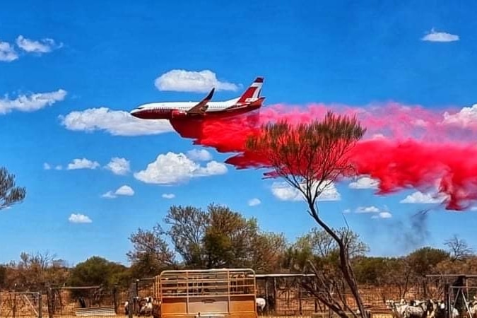 A white plane with red markings drops bright red liquid. In the foreground stockyards.