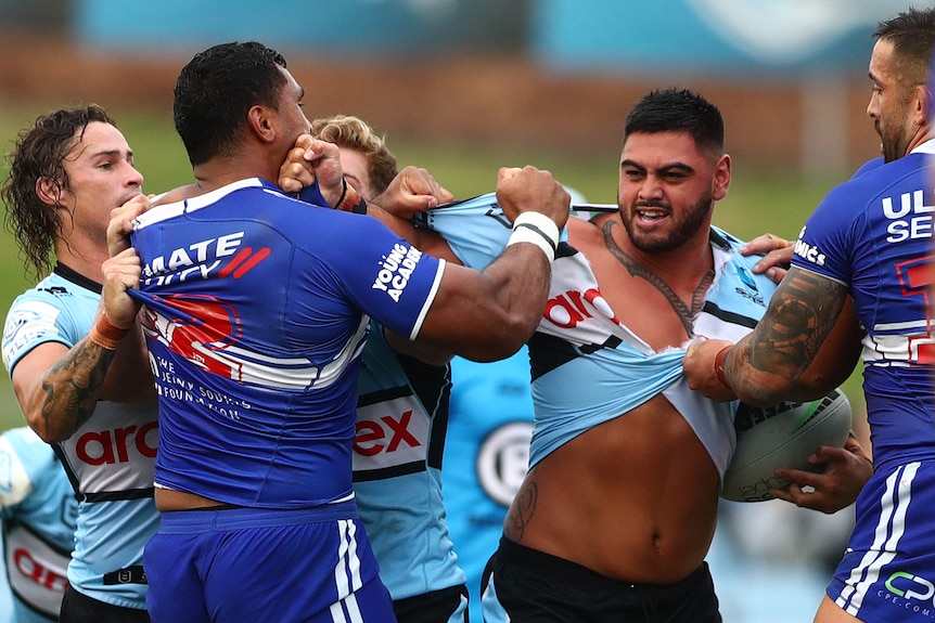 Cronulla Sharks player Royce Hunt has his jersey torn by Canterbury Bulldogs' Tevita Pangai Jr. Other players hold them both.