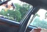 A screenshot of a video showing a police officer pointing a gun through a car window and the bloodied arm of a person inside.