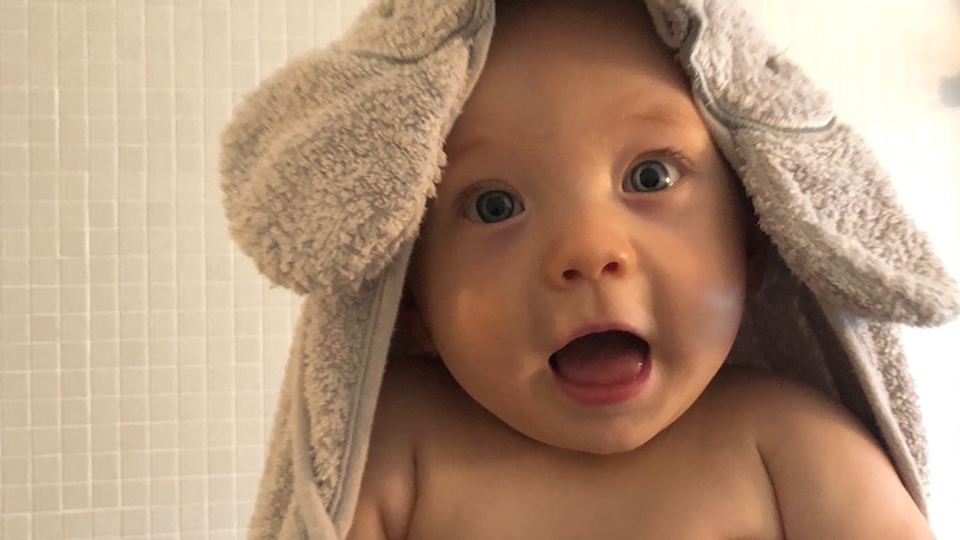 a baby boy looking into the camera, a towel loosely covering the top of his head and back