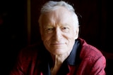 Playboy magazine founder Hugh Hefner smiles at the camera while wearing a red bathrobe.