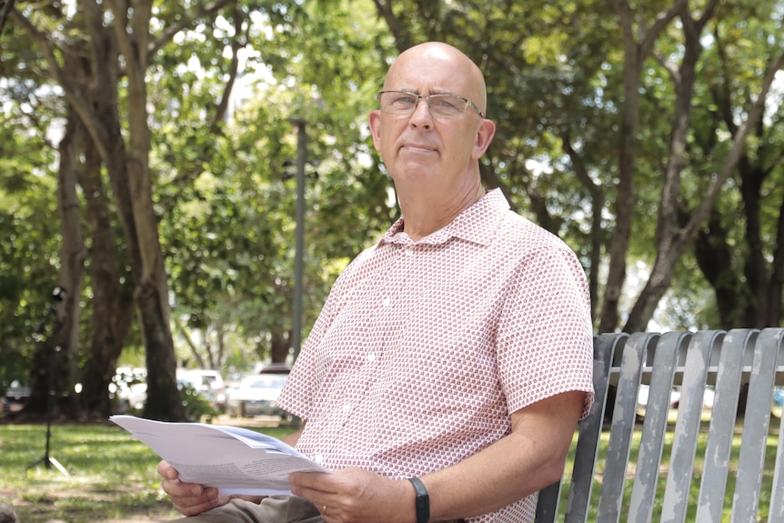 A man sits on a park bench holding a piece of paper. 