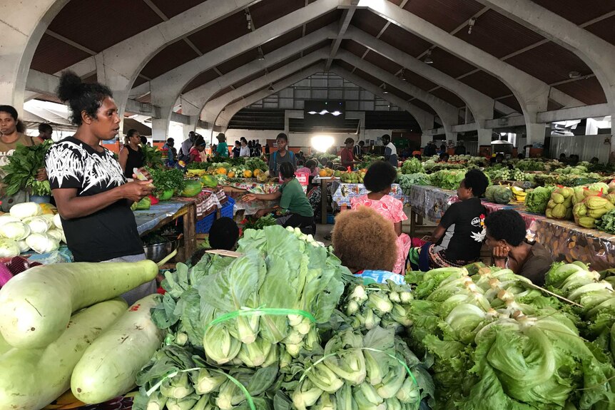 People sell fruit and vegetables in a large metal shed on the island of Efate, Vanuatu. There are some big green lettuces
