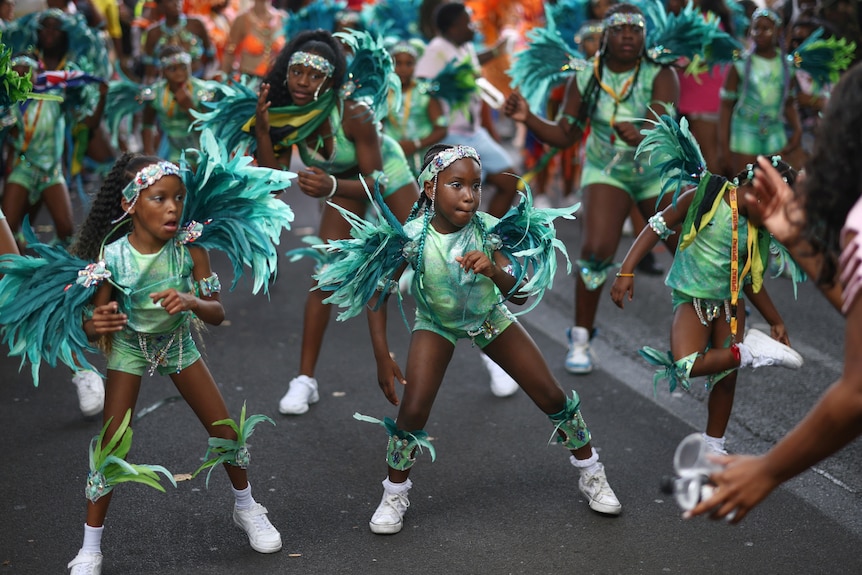 Young performers dressed in turquoise dance down a street.