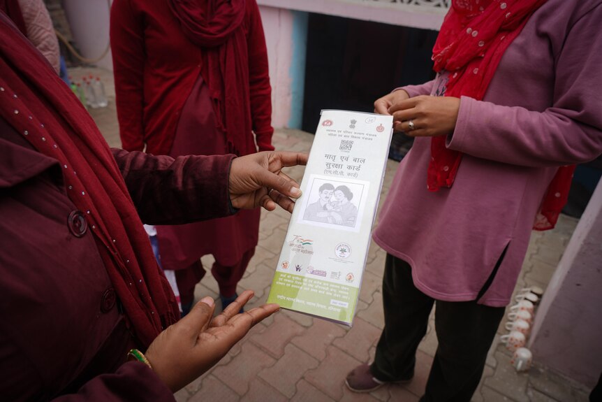A close-up on a group of women's hands show one woman offering a pamphlet about family planning