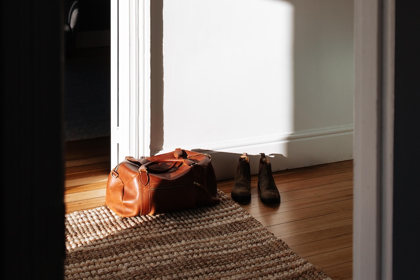 A duffel bag sits in a hallway alongside a pair of boots. 