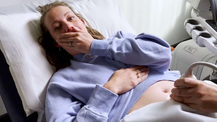 a woman lies on a hospital bed receiving an ultrasound, she looks happily at the screen perhaps she is pregnant