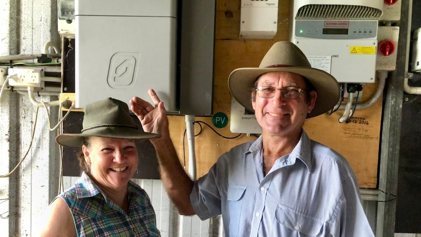 The couple stand in front of the boxes that regulate their off-grid power system.